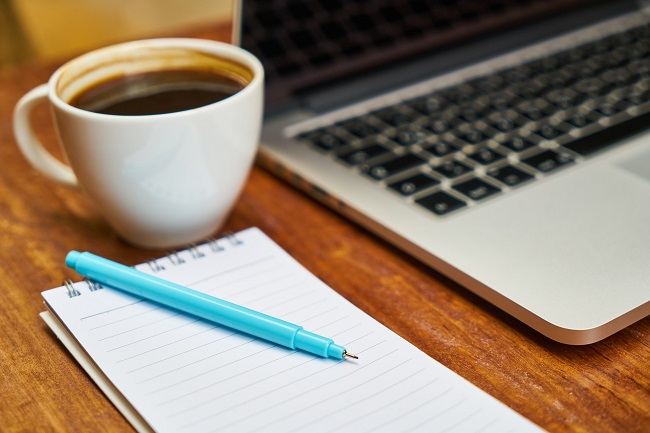 tasse de café posée à côté d'un ordinateur portable et d'un cahier avec un crayon
