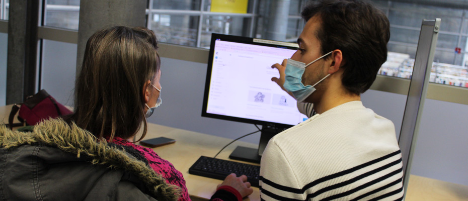 Arthur, conseiller numérique, en train d'accompagner une personne devant un ordinateur de la médiathèque.