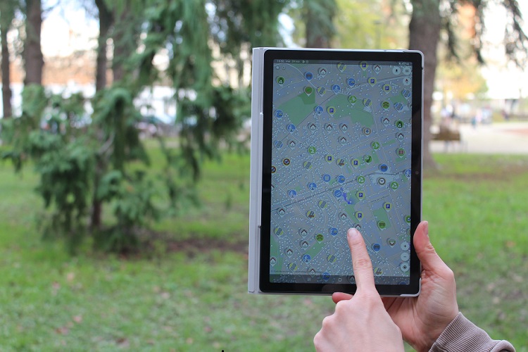 Une main tenant une tablette affichant l'application Streetcomplete, au deuxième plan des arbres