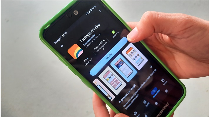 Une main tient un smartphone avec l'application Tout Apprendre 